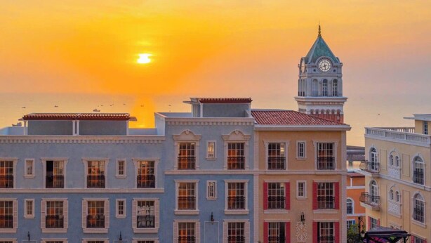 Una hilera de edificios históricos con una destacada torre de reloj, probablemente un hotel o edificio público, durante el atardecer.