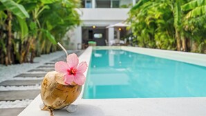 Una piscina en un entorno tropical, con un coco, una flor y una pajita.