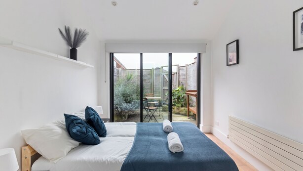 A modern bedroom with a large bed, a view of the backyard, and a sliding glass door.