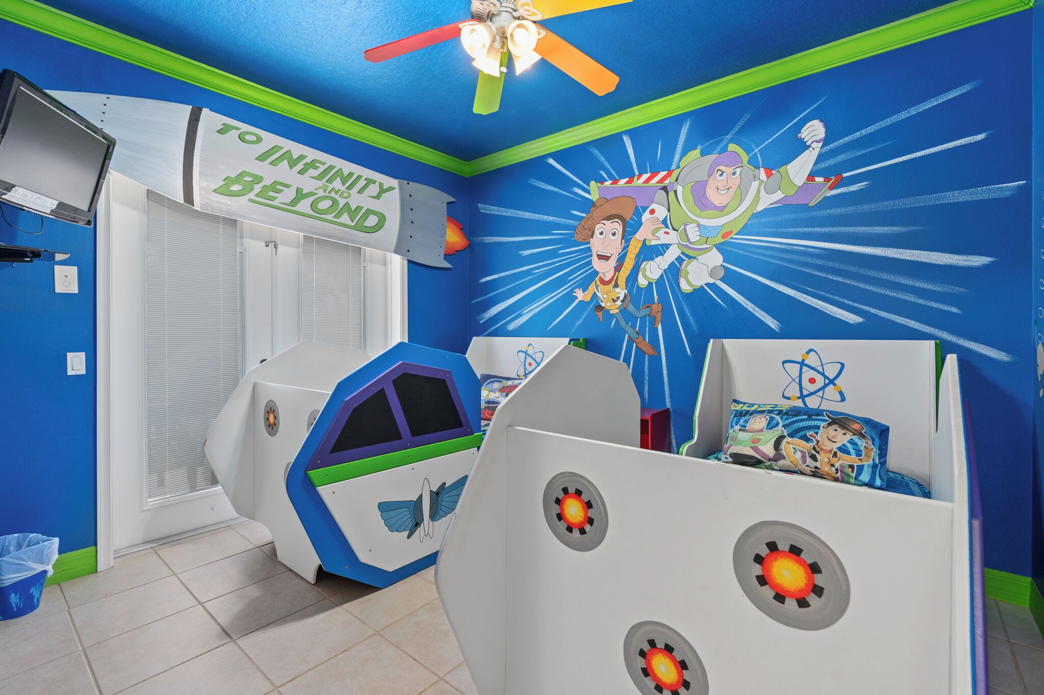 Una habitación infantil con una paleta de colores azul y verde, que presenta un mural de Woody y Buzz Lightyear, una cama con temática espacial y un letrero que dice 'Al infinito y más allá'.