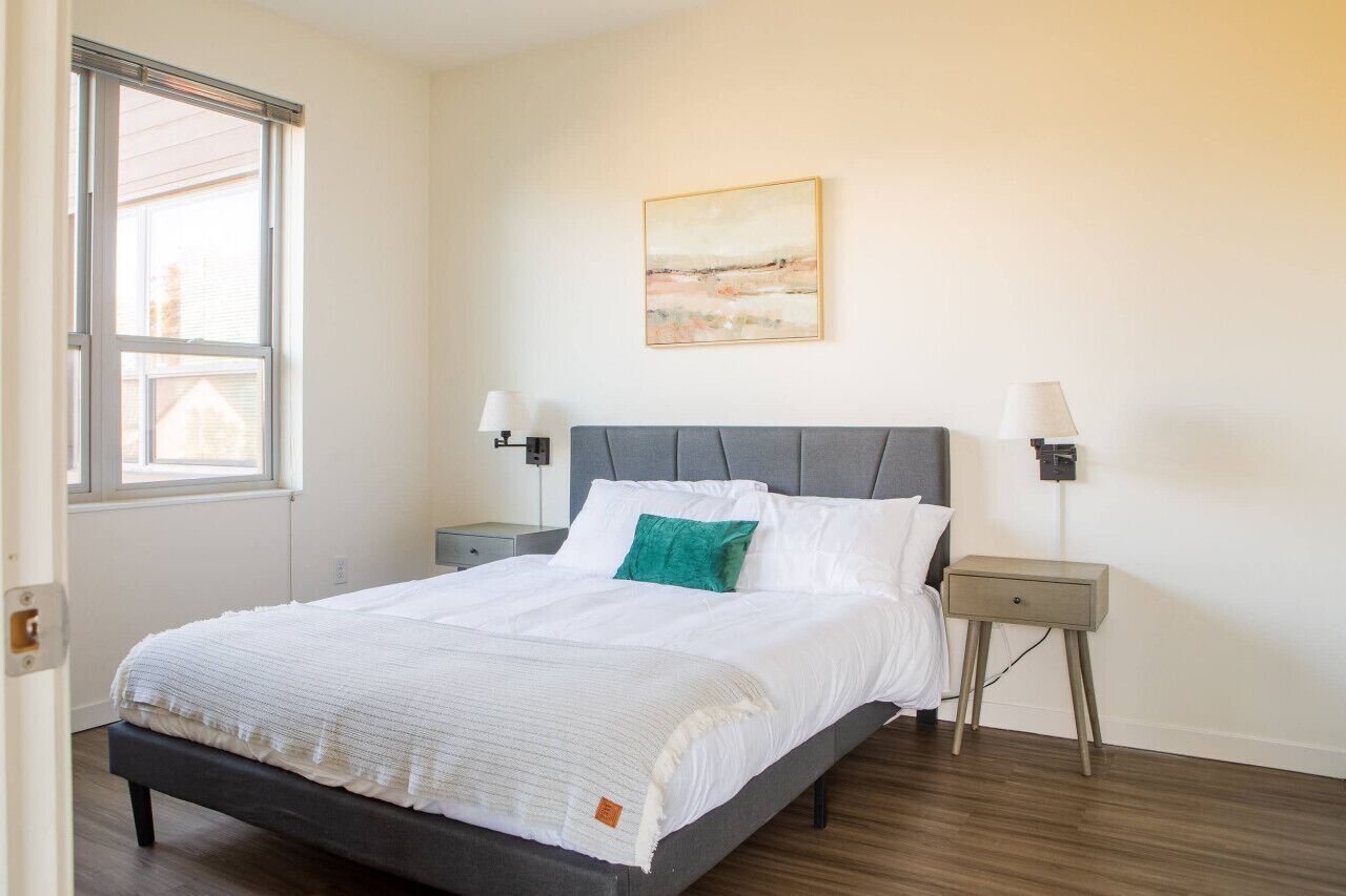 A bedroom with a bed, bedside tables, a window, and a painting on the wall.
