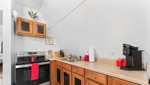 A modern kitchen with wooden cabinets, a stainless steel oven, a coffee maker, and a sink.