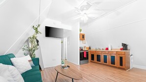 A modern living room with a green sofa, a wooden coffee table, and a kitchen area with wooden cabinets and a black refrigerator.