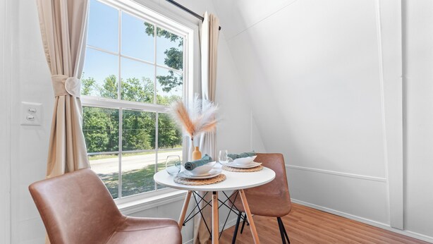 A dining area with a round table, two chairs, and a view of greenery outside.
