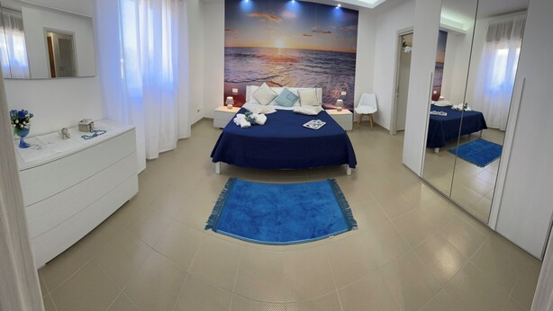 Een moderne hotelkamer met een groot bed, nachtkastje, dressoir, spiegel en een muurschildering van een zonsondergang.