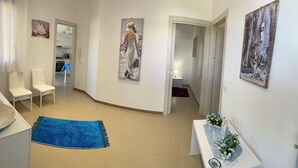 Een ruime hal met een blauw tapijt, witte stoelen en kunstwerken aan de wanden.