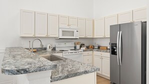 A modern kitchen with white cabinets, a granite countertop, a stainless steel refrigerator, a microwave, and a stove. - Highgate@Legacy Park, a 3 bed 2 bath pet friendly home within a gated community (Davenport)