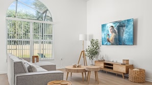 A modern living room with a large window, a grey sofa, a wooden coffee table, and a TV mounted on the wall. - Highgate@Legacy Park, a 3 bed 2 bath pet friendly home within a gated community (Davenport)