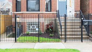 A two-story brick building with a corner entrance, a small front yard, and a black metal fence.