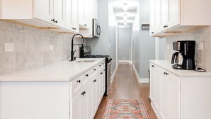 A kitchen with white cabinets, a stove, a coffee maker, and a patterned rug on the floor.
