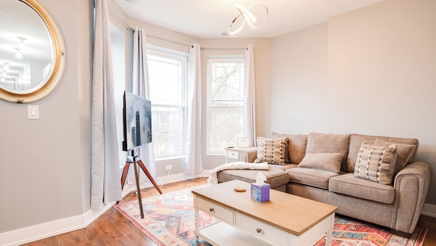 A living room with a sofa, a coffee table, a TV on a stand, and a patterned rug.
