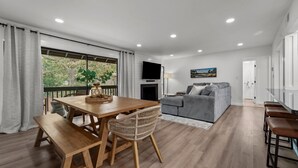 A modern living room with a wooden dining table, a grey sofa, and a TV mounted on the wall. - COMPLETELY REMODELED 3 BDR, 2 Bath, Golf Course View Condo (Pinehurst)
