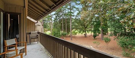A covered porch with wooden chairs and a view of a wooded area.