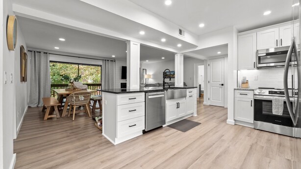 A modern kitchen with white cabinetry, stainless steel appliances, and a wooden dining area with a view of greenery. - COMPLETELY REMODELED 3 BDR, 2 Bath, Golf Course View Condo (Pinehurst)