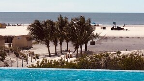 A clear blue pool with a view of a sandy beach and palm trees in the background.