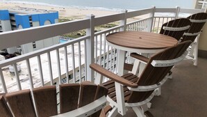 A balcony with wooden Adirondack chairs and a small round table.