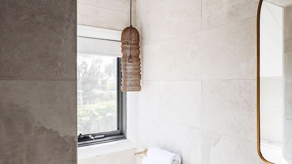 Un bagno con un'ampia finestra, un lampadario intrecciato e un portascopevoli bianco.
