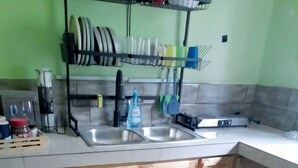 A kitchen with wooden cabinets, a double sink, and a dish rack with plates and bowls. -  2 bedrooms, 1 bathroom, kitchen, WiFi, and AC in Greendale, Spanish Town. (Spanish Town)
