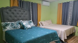 A bedroom with a large bed, a smaller bed, a tufted headboard, and a window with curtains. -  2 bedrooms, 1 bathroom, kitchen, WiFi, and AC in Greendale, Spanish Town. (Spanish Town)
