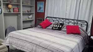 Une chambre à coucher comprenant un lit, un ventilateur de plafond, une étagère avec des objets décoratifs et une fenêtre avec des rideaux.