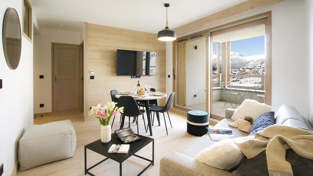 Un salon moderne comprenant un coin repas, un canapé, une table basse et offrant une vue sur un paysage enneigé grâce à de grandes fenêtres.