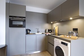 A compact kitchen with a Siemens oven, a sink, a coffee maker, a toaster, and a washing machine.