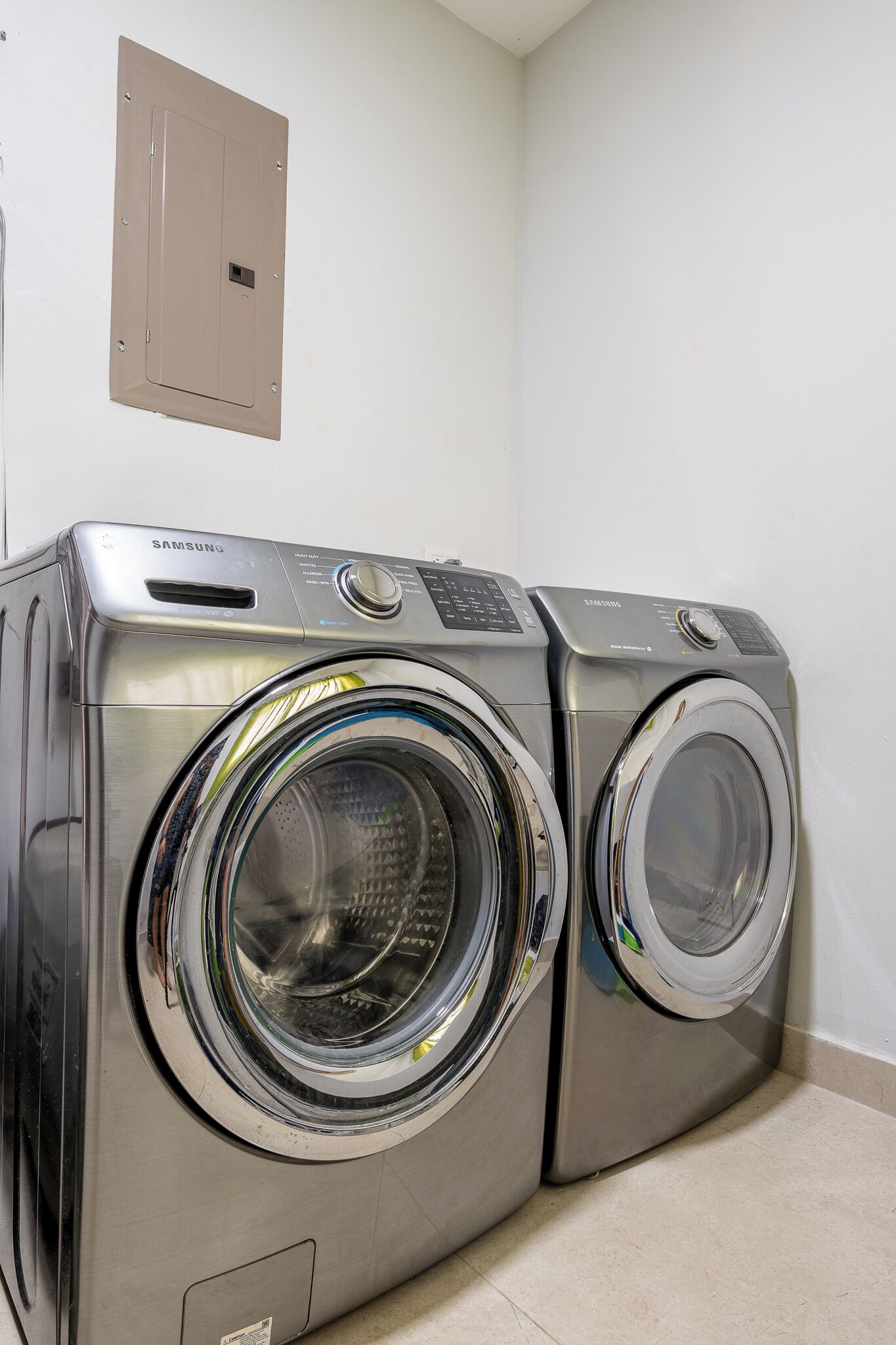 A Samsung front-loading washer and dryer stacked in a corner with a beige electrical panel on the wall.