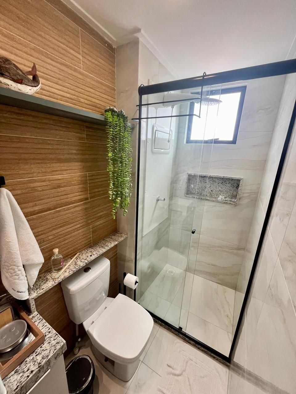 A modern bathroom with a glass-enclosed shower, a toilet, a sink, and a shelf with toiletries.