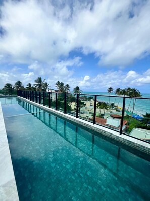 A long, clear infinity pool with a view of the ocean and palm trees. - Makadamia 107 (Ipojuca)