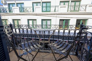 Un balcón con barandilla de hierro forjado y una silla plegable de metal.