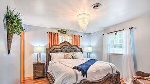 A bedroom with a wooden bed, a nightstand, a lamp, a hanging plant, and a window with curtains. - Relaxing 5-Bedroom Getaway with Saltwater Pool & Game Room Close to Hershey (Palmyra)