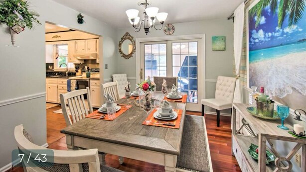 A dining area with a wooden table set for six, surrounded by white chairs. A chandelier hangs from the ceiling, and a painting of a beach is on the wall. - Relaxing 5-Bedroom Getaway with Saltwater Pool & Game Room Close to Hershey (Palmyra)