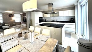 Een moderne keuken met een centraal eiland, witte kasten en een eethoek met een tafel voor vier personen.