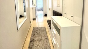 Een moderne gang met een witte wastafel, een spiegel en een deur naar een lichte kamer.