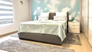Een slaapkamer met een bed, nachtkastje, dressoir en een raam met jaloezieën.