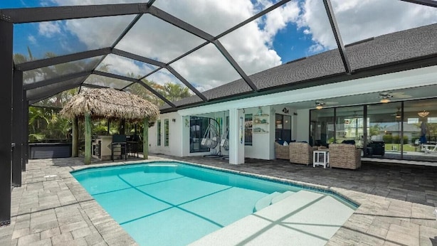 A covered outdoor swimming pool with a thatched-roof structure, stone flooring, and outdoor seating.