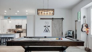 A pool table in a modern living room with a kitchen in the background.