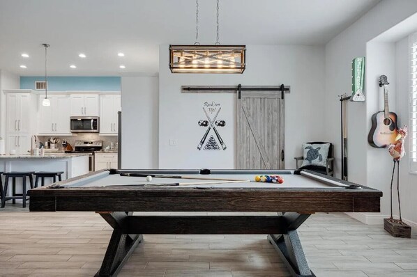 A pool table in a modern living room with a kitchen in the background.