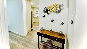 A hallway with a wooden table, a trash bin, and wall decorations including circular metallic objects and butterfly ornaments. - Modern Marvel in Windermere (Edmonton)