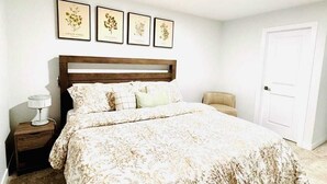 A bedroom with a large bed, a nightstand, a chair, and three framed botanical prints on the wall. - Modern Marvel in Windermere (Edmonton)