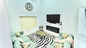 A living room with a sofa, a coffee table, a flat-screen TV, a fireplace, and a dartboard. - Modern Marvel in Windermere (Edmonton)