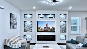 Una sala de estar moderna con un televisor de pantalla plana montado en la pared, sofás grises, una mesa de centro y decoración mural.