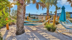 Zona de playa arenosa con hamacas y sillas de descanso, palmeras y cielo despejado.
