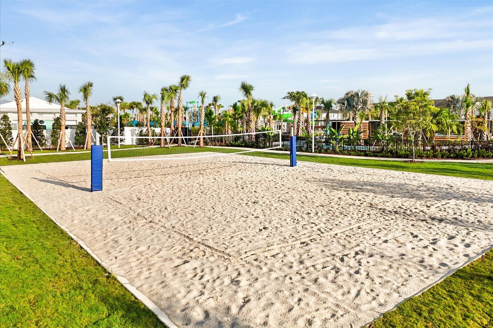 Una cancha de voleibol de arena, con una red, rodeada de palmeras y una valla.