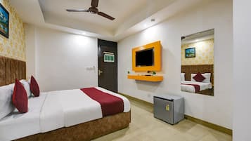A hotel room with a bed, a ceiling fan, a TV mounted on the wall, a small fridge, and a door with a sign.