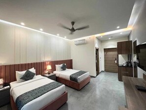 A hotel room with two beds, a desk, a TV, and a ceiling fan. - Hotel Happy Stay - Delhi Airport (New Delhi)