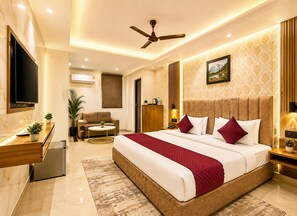 A modern hotel room with a large bed, a desk, a sofa, and a TV. - Hotel Happy Stay - Delhi Airport (New Delhi)