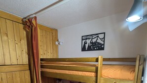 Ein Stockbett mit roter Matratze, eine hölzerne Sitzbank und eine Wandleuchte.