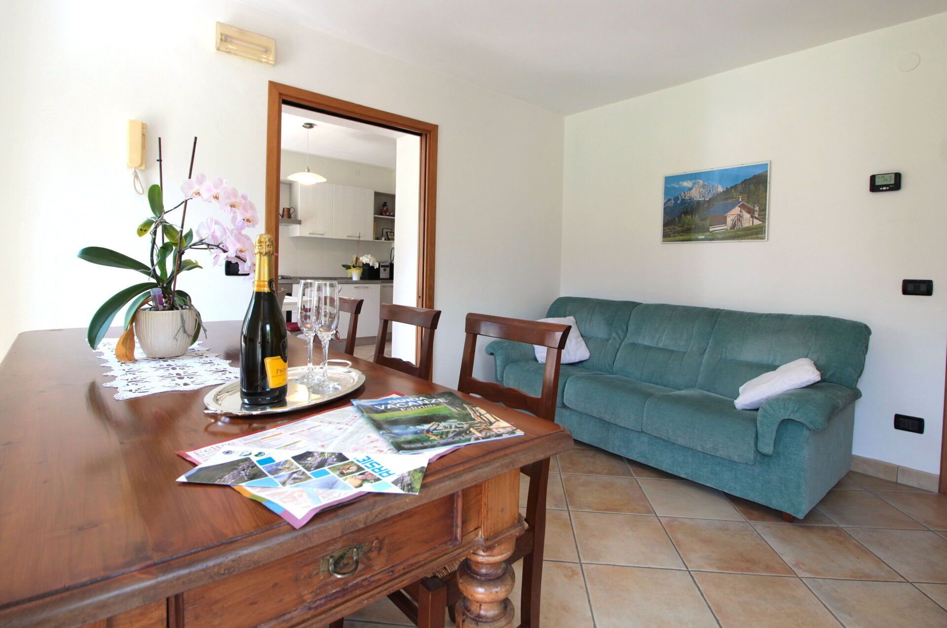 A dining area with a wooden table, a green sofa, a potted orchid, and a bottle of champagne.