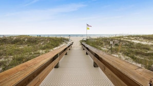 A wooden boardwalk leading to a beach with a flag. - Phoenix 8 8904- Sand Shells Sun Can Rent at 18 3 Bedrooms 2 Baths (Orange Beach)